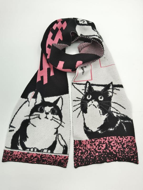 Gestrickter Schal mit schwarz-weißen Smoking-Katzen-Illustrationen und pinkfarbenen geometrischen Akzenten, aufgerollt auf hellem Hintergrund