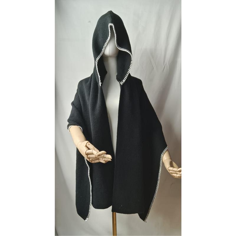 Eleganter schwarzer Kapuzenponcho aus Wolle mit kunstvollem weißem Bordürenmuster auf Schneiderpuppe mit Holzhänden