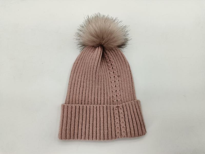 Puderrosa Strickmütze mit großem fluffigem Kunstfell-Pompom, auf weißem Hintergrund fotografiert