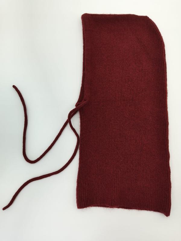Weinrote gestrickte Sturmhaube mit feinem Rippenmuster und langen Schnürbändern, von oben fotografiert auf hellem Untergrund