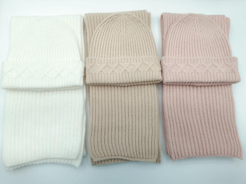 Drei aufeinander abgestimmte Zopfstrick-Beanie und Rippschal Sets in Elfenbein, Taupe und Altrosa nebeneinander auf weißem Hintergrund