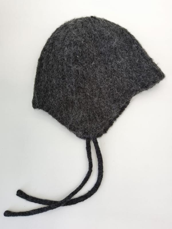 Handgestrickte Babymütze aus anthrazitgrauer Filzwolle mit Ohrenklappen und geflochtenen Bindeschnüren, auf weißem Hintergrund