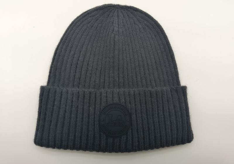 Anthrazitgraue Rippenstrick-Beanie mit gefaltetem Rand und rundem Gummi-Logoaufnäher mit der Aufschrift Change Is Possible, Flachaufnahme auf weißem Untergrund