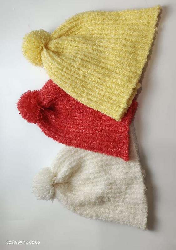 Drei flauschige Chenille-Strickmützen mit Bommel in Gelb, Rot und Weiß übereinandergestapelt vor weißem Hintergrund
