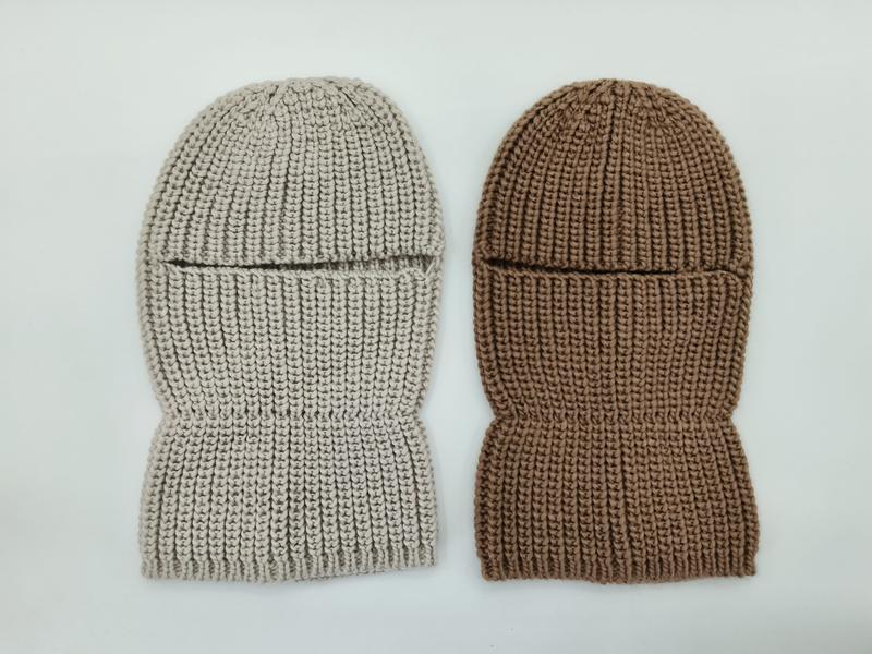 Zwei grob gestrickte Ganzkopfmasken flach liegend – eine in Hellbeige, eine in Warmbraun – mit Augenschlitz und Rippenstruktur