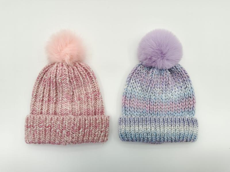 Zwei Grobstrick-Mützen mit Kunstfell-Pompons nebeneinander: eine in Rosa-Melange, die andere in Lavendel-Blau-Batik-Optik auf weißem Hintergrund