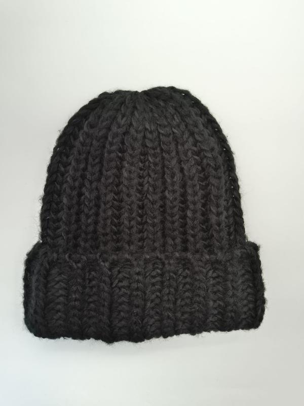 Schwarze grob gestrickte Beanie mit breitem Umschlagbund, handgemacht wirkend, flach auf weißem Hintergrund fotografiert