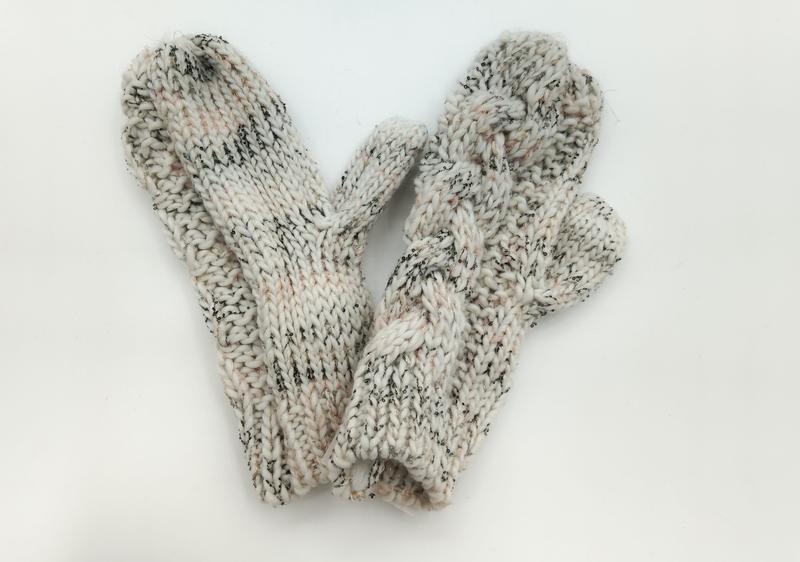 Ein Paar cremefarbene Woll-Fäustlinge mit schwarzem Tweed-Sprenkelmuster und ausgearbeiteter Daumennaht, flach ausgelegt auf weißem Hintergrund