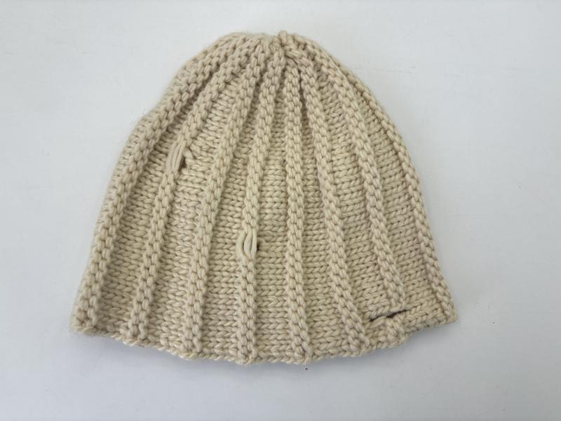 Draufsicht einer cremefarbenen, grob gerippten Strickmütze aus natürlichem Elfenbein-Garn, gefaltet zur Ansicht der Stricktextur
