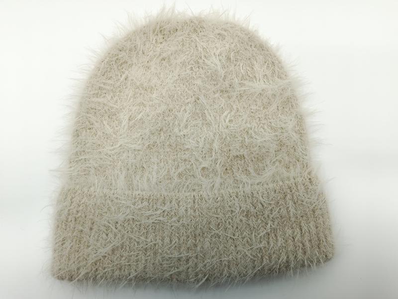 Beige-cremefarbene Mütze aus Eyelash-Garn mit flauschiger Fadenstruktur und Rippbündchen auf weißem Hintergrund