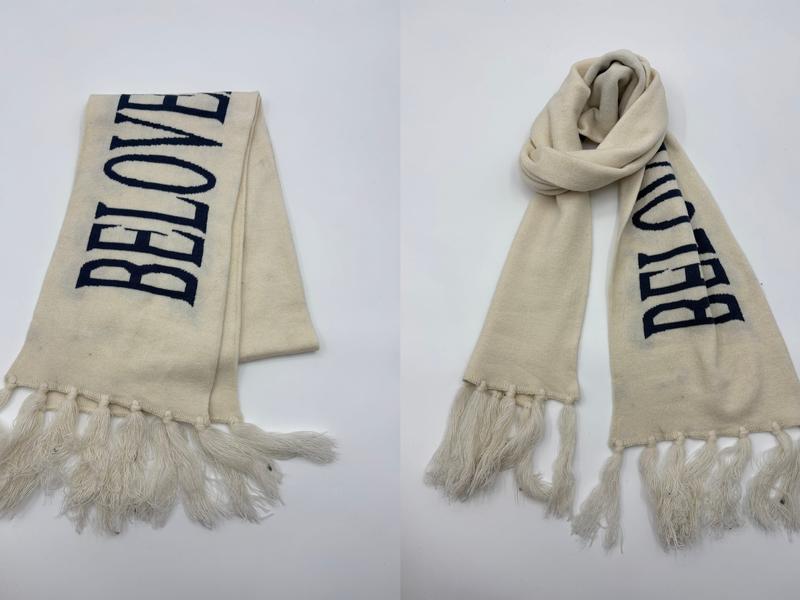 Heller Strickschal mit eingestricktem dunkelblauen Schriftzug und langen Quastenenden, flach ausgelegt und als Halsschal drapiert