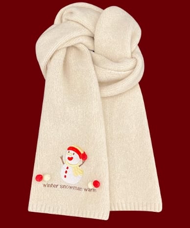 Weicher cremefarbener Strickschal mit aufgesticktem Schneemann-Motiv und roten Bommeln als Dekoration, auf dunkelrotem Hintergrund zusammengelegt