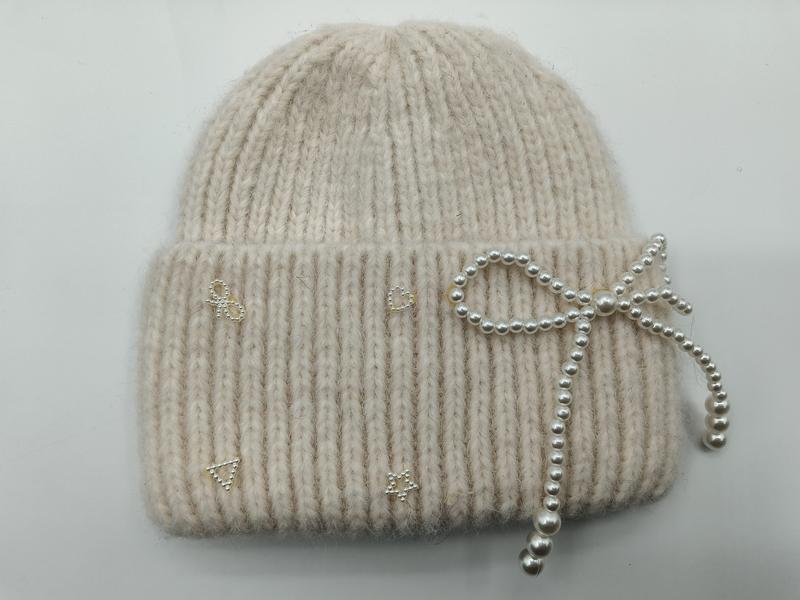 Gestrickte Wintermütze in Creme mit feiner Rippenstruktur, verziert mit einer Perlenschleife und funkelnden Strass-Akzenten am Umschlag