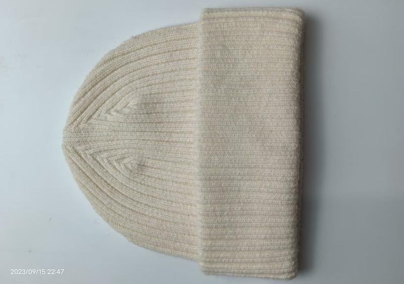 Cremeweiße Rippenstrickmütze mit umgeschlagenem Bündchen auf weißer Fläche, klassische Stricktextur in Naturweiß