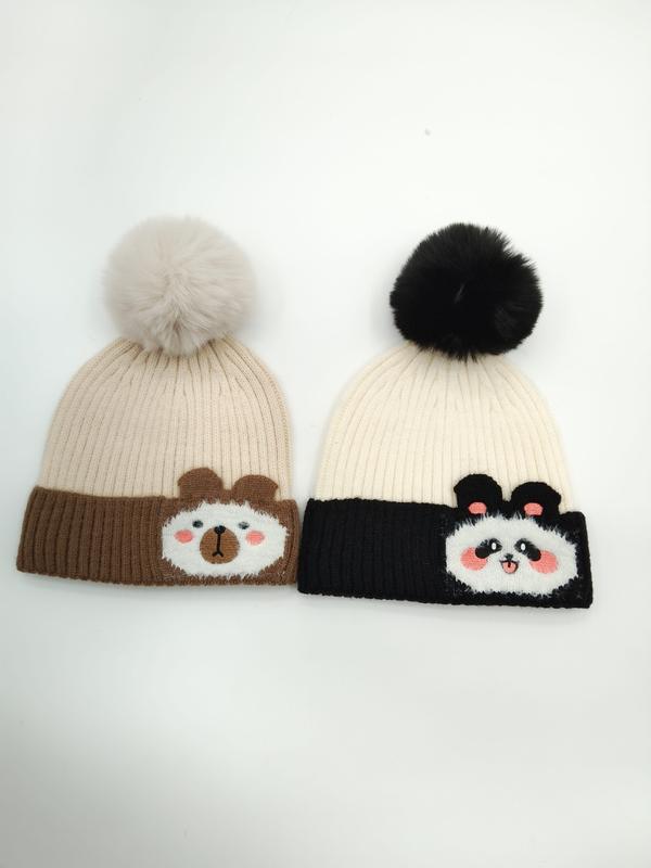 Zwei Strickmützen mit Bommeln: hellbraune Bärenmütze mit Cartoon-Bärengesicht und schwarz-cremefarbene Pandamütze mit Panda-Applikation