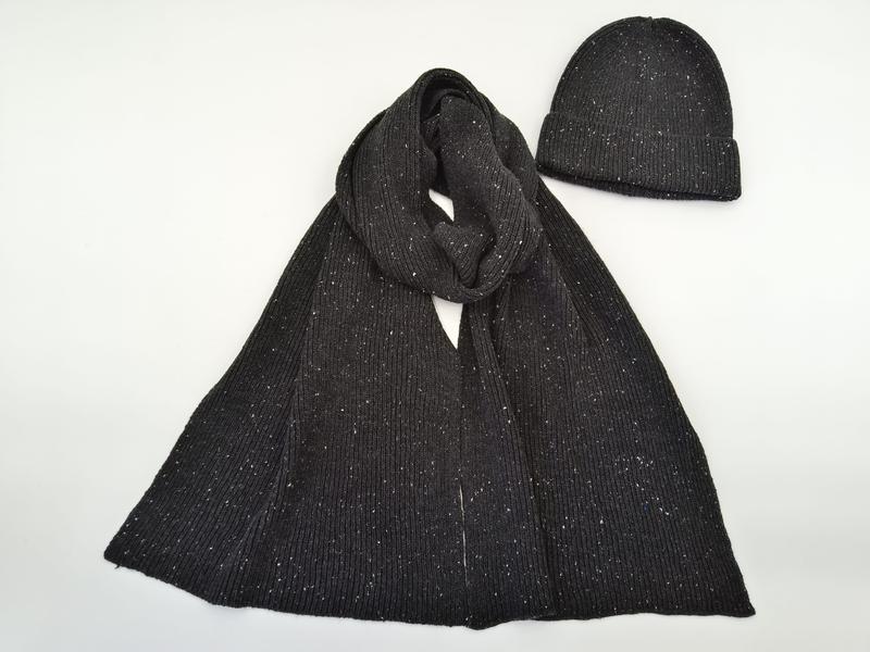 Anthrazitfarbener Rippstrickschal locker drapiert neben passender Beanie-Mütze mit weißem Fleckenmuster