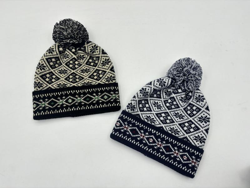 Zwei Strickbommelmützen im skandinavischen Fair-Isle-Muster auf weißem Grund: eine in Schwarz-Creme, eine in Marineblau-Weiß mit Schneeflocken-Rautenmotiv