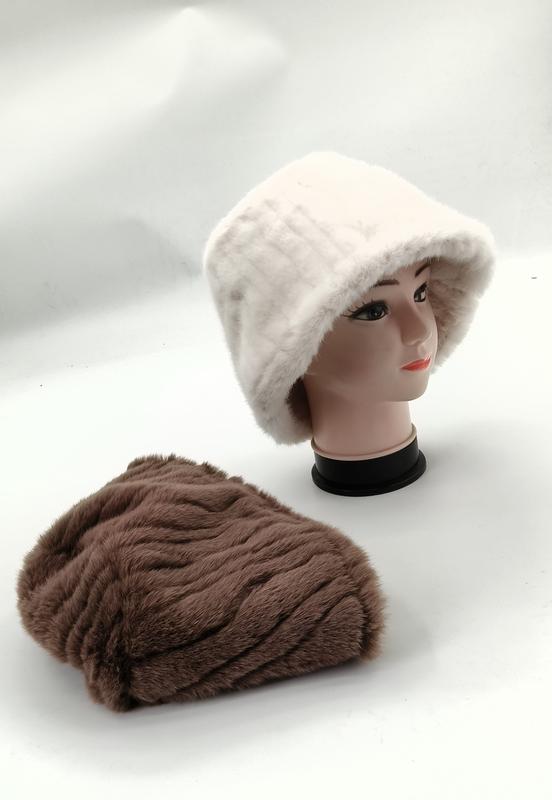 Weißer Kunstfell-Bucket-Hat auf Schaufensterkopf neben flach liegender brauner Plüschmütze auf weißer Fläche
