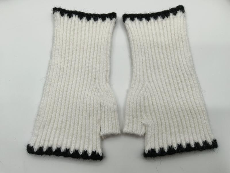 Paar weiße Rippenstrick-Fingerhandschuhe mit schwarz-weißem Zickzack-Abschlussband oben und unten, flach auf weißem Hintergrund