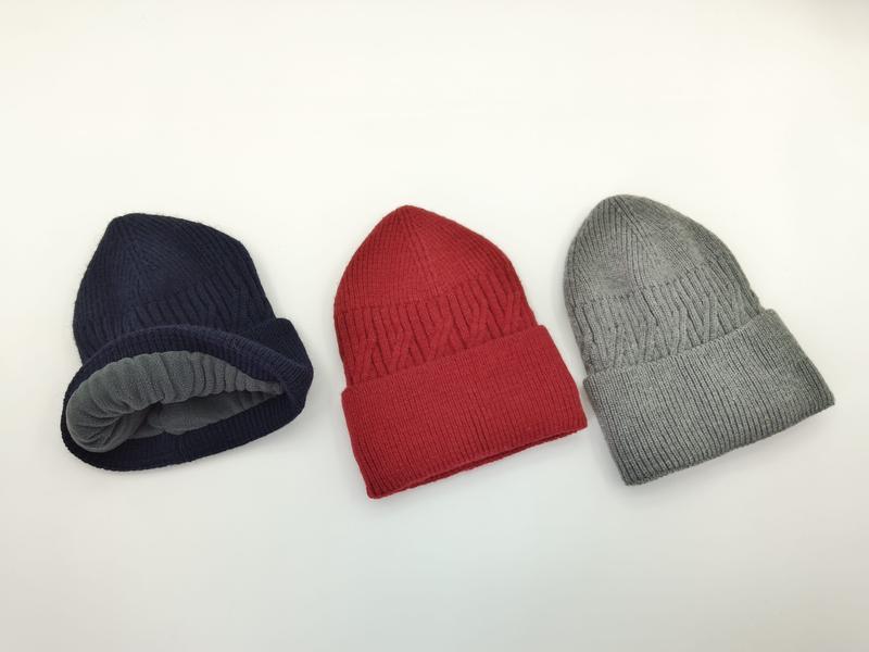 Drei gerippte Strickmützen in Dunkelblau, Rot und Grau auf weißem Hintergrund, Marineblaue Mütze zeigt graues Fleece-Innenfutter