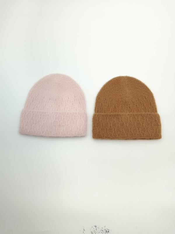 Zwei flauschige Wintermützen mit Umschlagbund nebeneinander, eine in zartem Rosa und eine in warmem Kamelbraun, Draufsicht auf weißem Untergrund