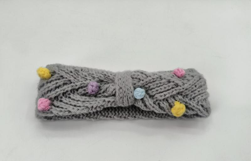 Gestricktes Stirnband in Grau mit Zopfmuster und farbenfrohen Mini-Pompons in Gelb, Rosa, Lila und Blau sowie dekorativem Schleifendetail in der Mitte