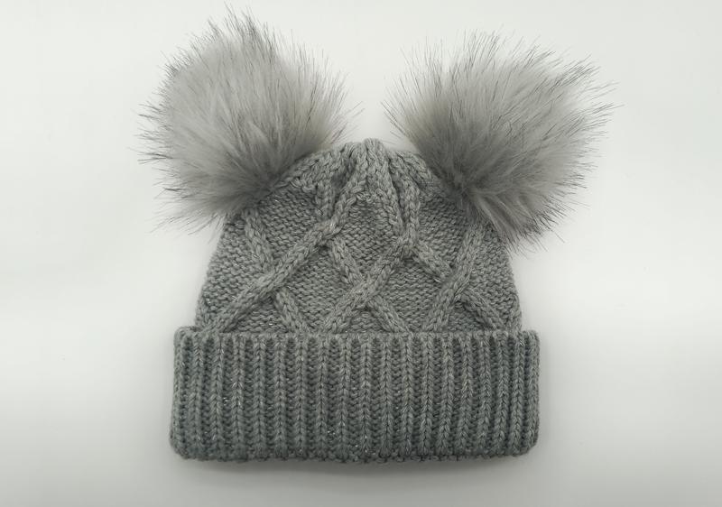 Graue Wintermütze im Zopfstrickmuster mit zwei flauschigen Kunstfell-Pompons oben und geripptem Umschlag, Flachaufnahme auf weißem Hintergrund