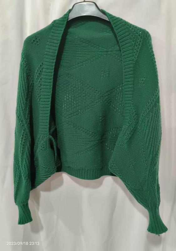 Offener smaragdgrüner Strickjacke mit Durchbruch-Rautenmuster und Rippenbündchen auf einem Kleiderbügel vor weißem Hintergrund