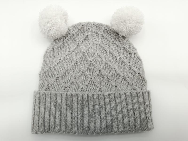 Hellgraue Strickmütze für Babys mit zwei flauschigen Pompons und Umschlagbündchen, Detailaufnahme auf hellem Untergrund