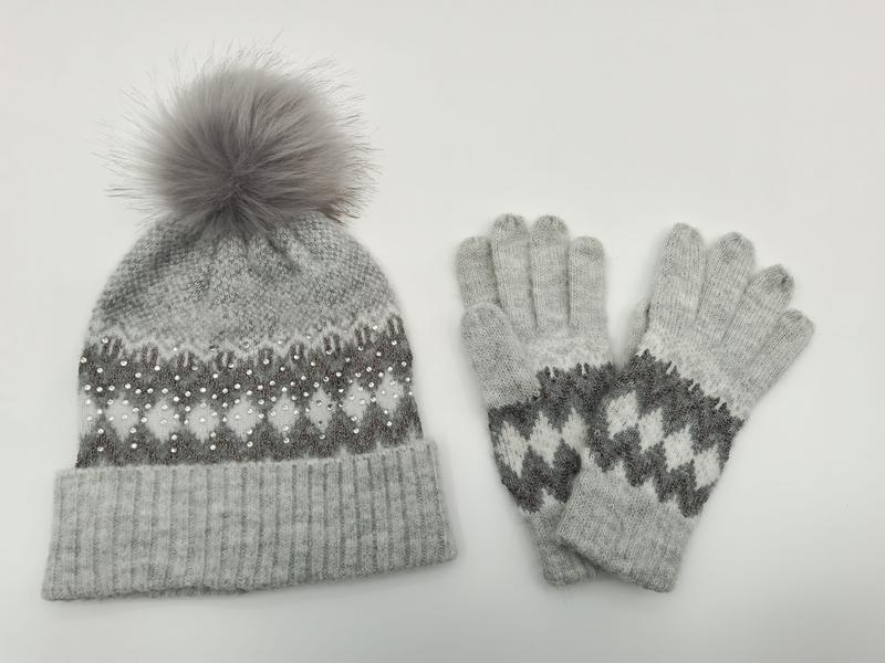 Graue Fair-Isle-Strickmütze mit Kunstfell-Bommel und Perlenapplikationen neben passenden Strickhandschuhen als Set