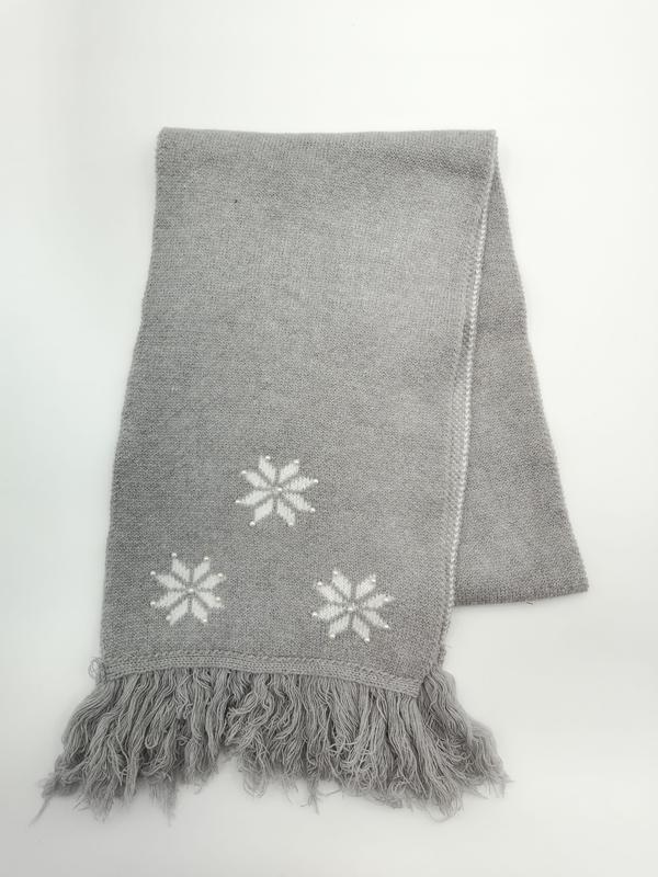 Gefaltete graue Strickdecke mit eingestrickten weißen Schneeflockenmotiven und Fransensaum auf weißem Untergrund