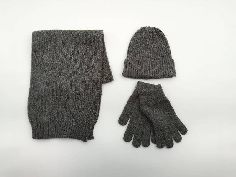 Flach drapiertes graues Strick-Accessoire-Set mit Schal, Beanie-Mütze und Handschuhen auf weißem Untergrund