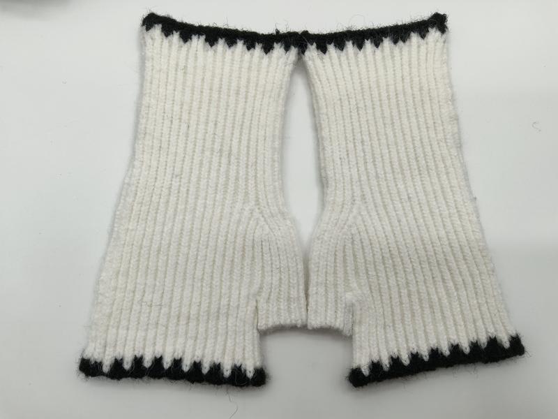 Draufsicht auf handgestrickte weiße Rippenstrick-Fingerhandschuhe mit schwarzen Kontrastbündchen an Handgelenk und Fingeröffnungen