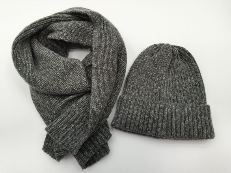 Grau melierter Rippenstrick-Beanie und passender langer Strickschal, flach auf weißem Hintergrund ausgelegt