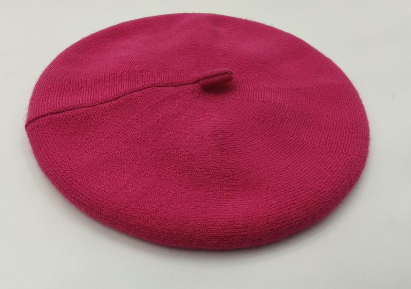Knallpinkfarbene feingestrickte Baskenmütze mit Ripprand und Mittelstielo, flach auf weißem Hintergrund fotografiert