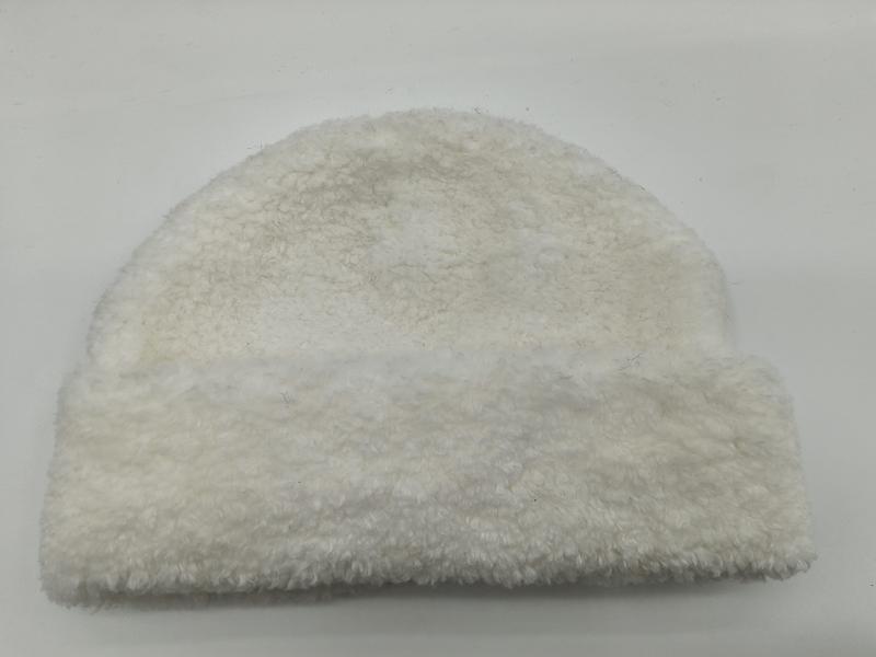 Cremefarbene Plüschmütze aus Sherpa-Fleece mit lockiger Teddystruktur, auf hellem Hintergrund liegend – flauschiges Winteraccessoire