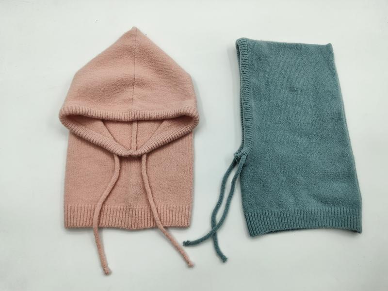 Zwei gestrickte Baby-Sturmhauben flach ausgelegt – eine in Altrosa geöffnet und eine in Petrol gefaltet, beide mit Kordelverschluss