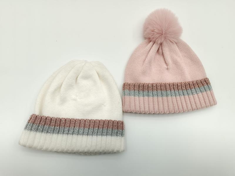 Zwei Rippenstrick-Beanies in Weiß und Rosa mit schimmernden Metallic-Streifen am Umschlag – pinke Mütze mit Kunstfell-Bommel obenauf