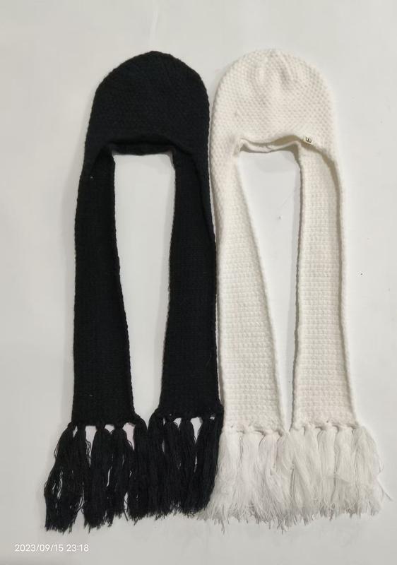 Zwei gestrickte Kapuzenmützen mit langen Quastenenden in Schwarz und Weiß flach liegend, Balaclavastil mit Ohrenschutz