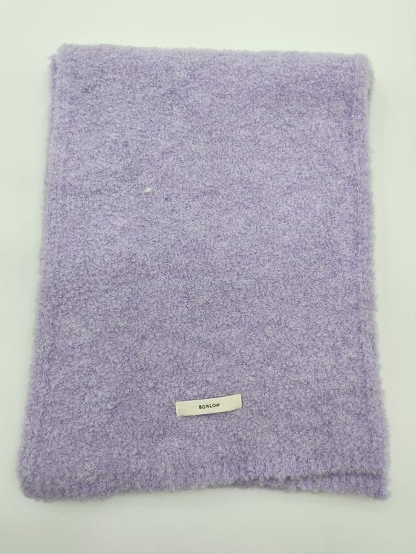 Gefaltete weiche Kuscheldecke in Fliederviolett mit Boucle-Oberfläche und kleinem Etikett auf weißem Hintergrund