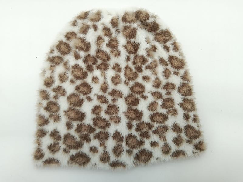 Weiche weiß-braune Kunstfell-Mütze mit Leopardenmuster, flach auf hellem Untergrund fotografiert