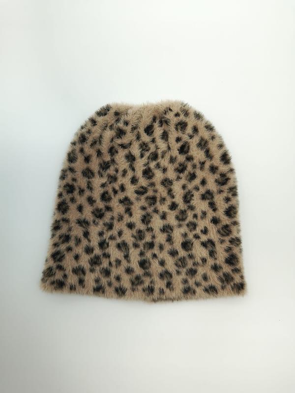 Draufsicht auf eine flauschige Strickmütze mit Leopardenmuster in Sandtönen und dunklen Flecken auf weißem Untergrund