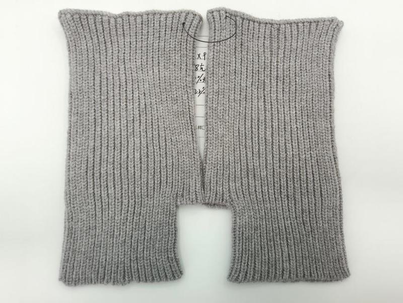 Ein Paar hellgraue fingerlose Strickhandschuhe mit Rippenmuster, flach liegend auf weißem Hintergrund, offene Fingeröffnungen gut sichtbar
