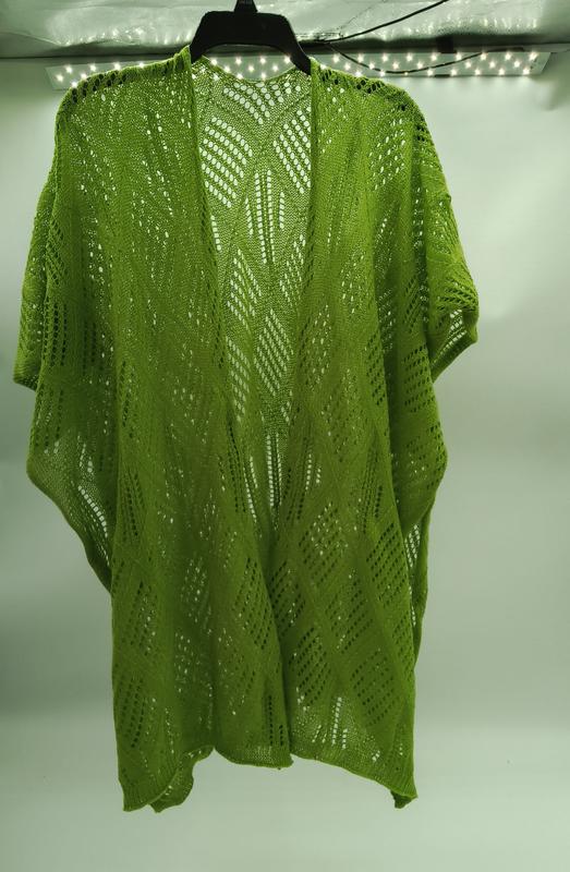 Limettengrüner Häkel-Kimono mit Rauten-Chevron-Muster auf schwarzem Kleiderbügel vor weißer Wand
