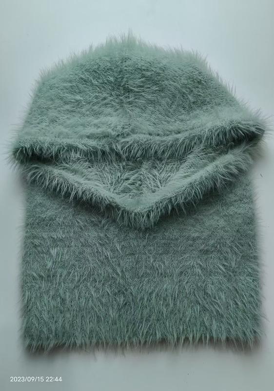 Gefaltete mintgrüne Flauschgarn-Balaclava mit passendem Schlauchschal auf weißem Hintergrund, Eyelash-Yarn-Textur sichtbar