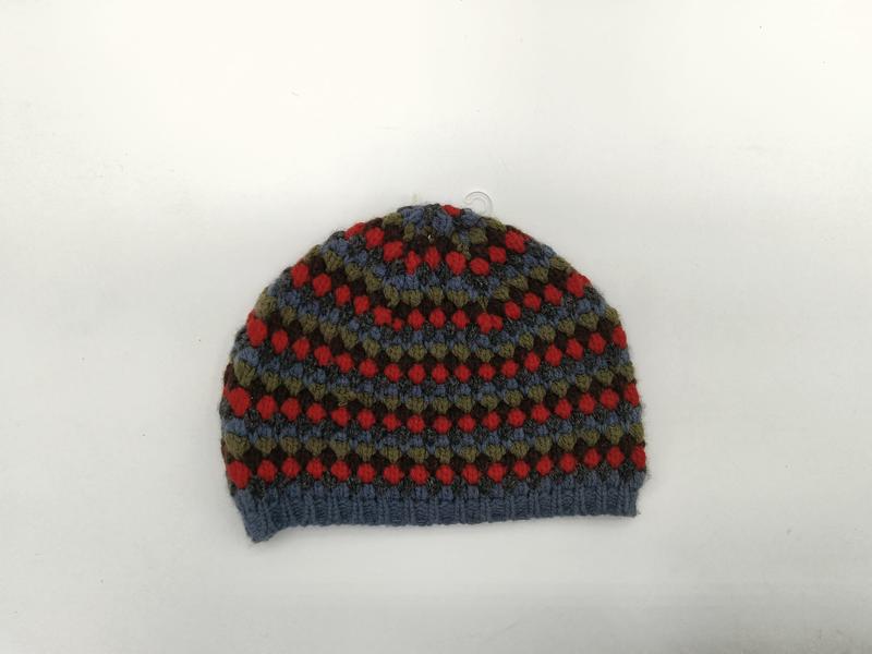 Handgestrickte Bommelmütze mit traditionellem Fair-Isle-Norwegermuster in den Farbtönen Blau, Rot, Olivgrün und Braun auf weißem Hintergrund