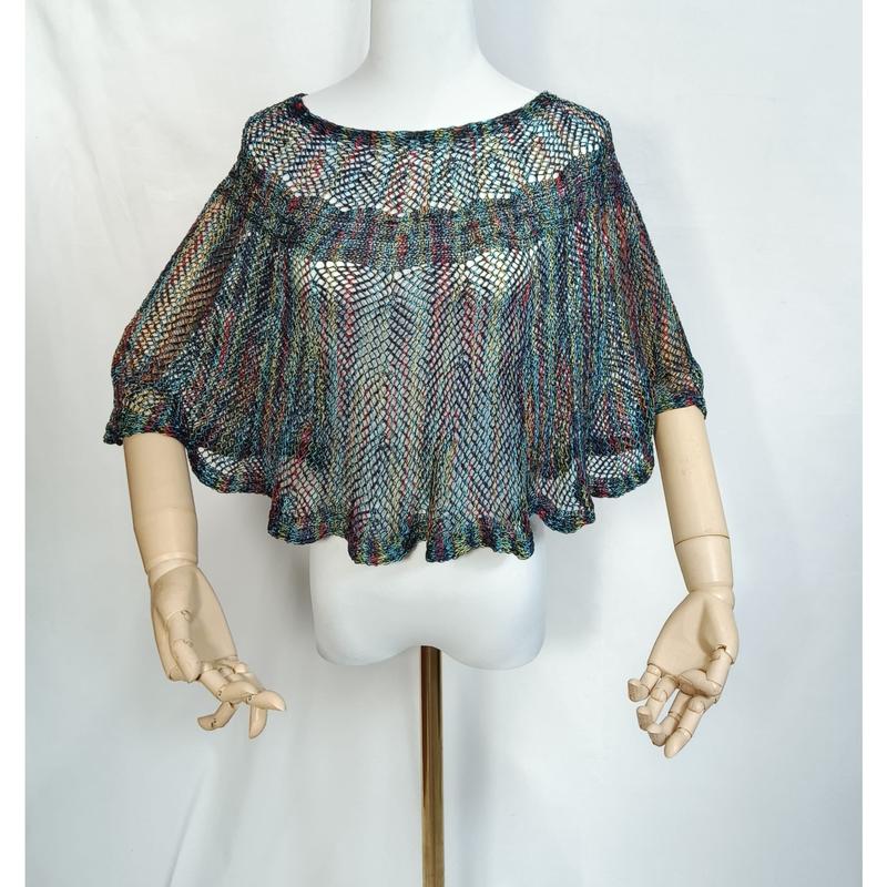 Mehrfarbiger Häkelponcho mit offenem Webmuster auf Schaufensterpuppe mit gegliederten Holzhänden, Regenbogen-Mesh-Stil