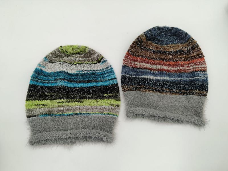 Zwei flauschige Strickmützen mit buntem Streifenmuster, eine in Blau-Grün-Tönen und eine in Rot-Braun-Tönen, beide mit grauem Kunstfellbündchen