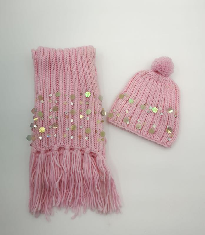 Pinker Rippenstrick-Winterschal mit Fransen und Pailletten, kombiniert mit passender Bommelmütze auf weißem Hintergrund
