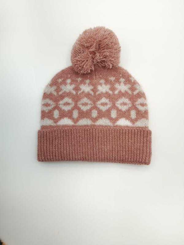 Rosafarbene Strickmütze mit weißen geometrischen Schneeflocken-Ornamenten und flauschigem Bommel, Produktfoto auf hellem Hintergrund